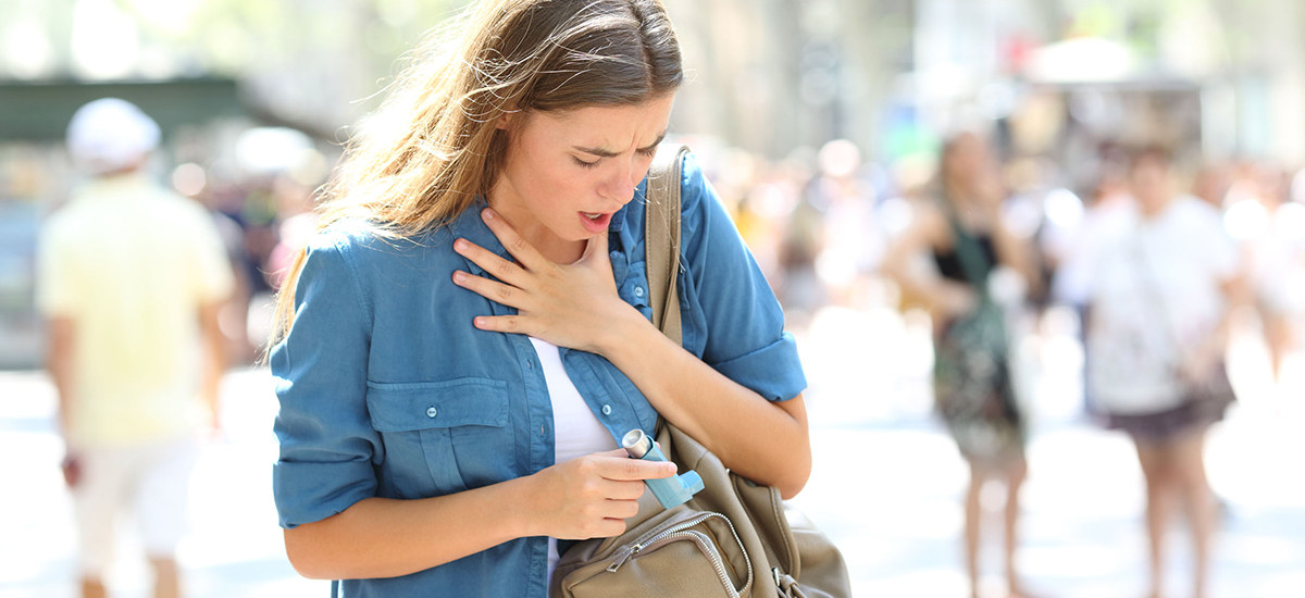 Slide Image of a young woman holding her chest with her left hand whilst removing a blue inhaler from her handbag