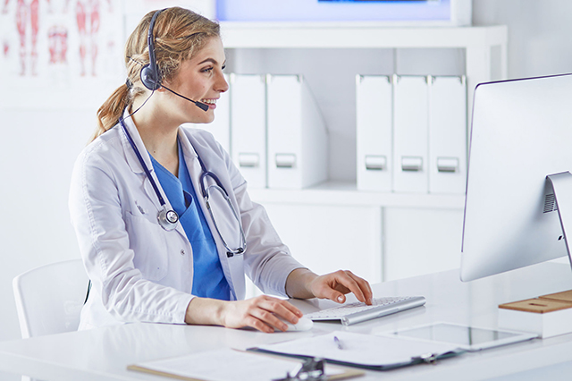 Image of a doctor looking at a computer screen whilst  talking to  a patient  via headset
